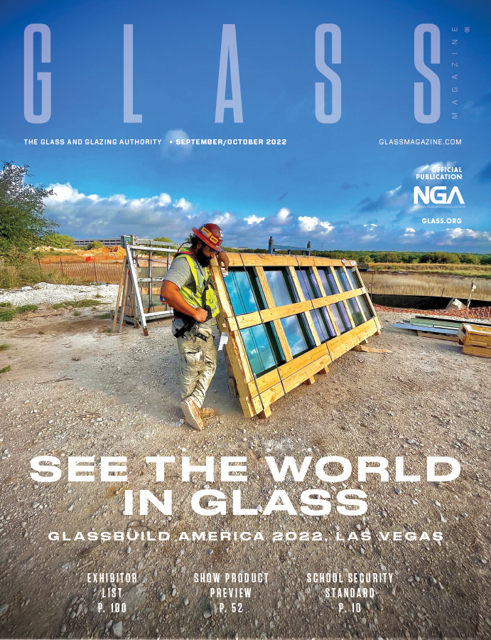 a construction worker n a hard hat leans on a framed window ready for installation on the front cover of the September October issue of Glass Magazine