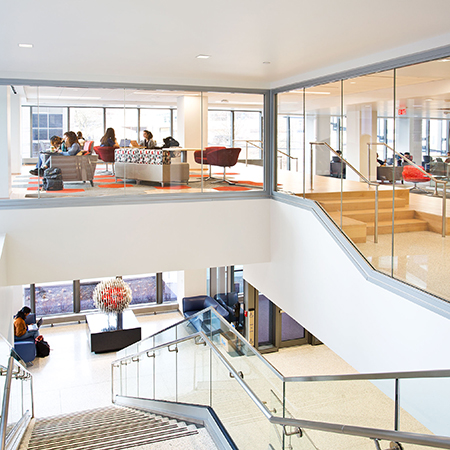 an interior photo of an office with glass railings along a staircase and glass walls between a hallway and meeting rooms