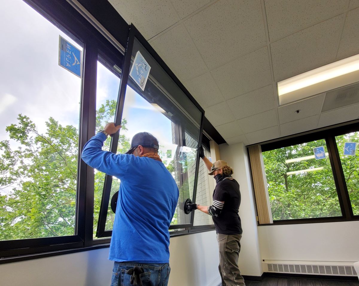 two workers lift window into place from inside office