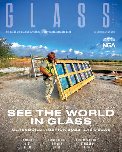 a construction worker n a hard hat leans on a framed window ready for installation on the front cover of the September October issue of Glass Magazine