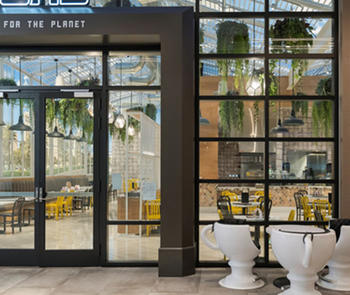 an exterior photo of the glass entry door and front window of a coffee shop with a white table and chairs on the sidewalk