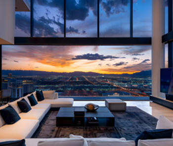 an interior view looking from a hillside through large windows at a sunset over an illuminated city skyline 